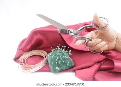 Hands are using scissors to cut a damask sateen fabric with a tape measure and a green needlepoint pillow.