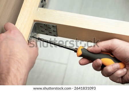 Hands using a screwdriver to fasten a metal bracket to a wooden frame