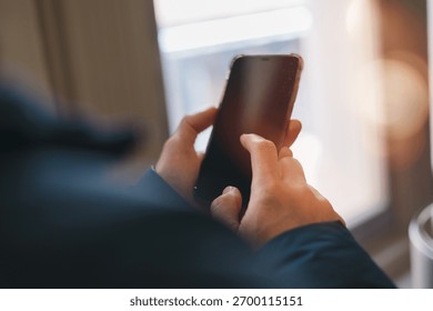 hands using smartphone indoors, browsing or texting with blurred background and warm light. Great for lifestyle, communication, technology, mobile app digital connection content.
