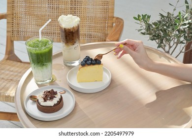 Hands using a spoon to scoop a cake surrounded by tea, coffee and cakes.