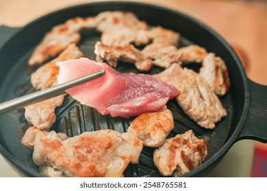 Hands using stainless steel chopsticks, there is raw pork or pork barbecue grilled on a pan, eaten in Asian style. - Powered by Shutterstock