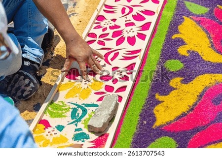 Hands using a stencil to create a detailed design on a vibrant sawdust carpet during Semana Santa in Antigua Guatemala. A moment of devotion and artistry.