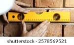 Hands using a yellow level tool on a brick wall, ensuring alignment. The level tool is crucial for precise construction and brickwork. Accurate leveling is key. House renovate and construction.