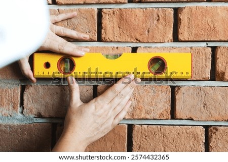 Hands using a yellow level tool on a brick wall. Level tool ensures bricks are aligned. Brick wall construction with level tool for precision. House renovate and construction concept.