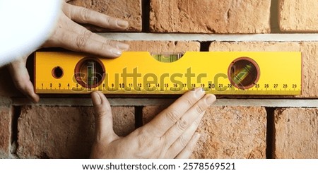 Hands using a yellow level tool on a brick wall, ensuring alignment. The level tool is crucial for precise construction and brickwork. Accurate leveling is key. House renovate and construction.