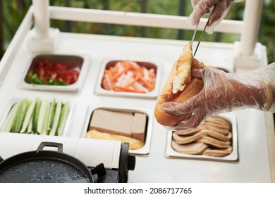 Hands Of Vendor Wearing Protective Gloves When Making Sandwich With Fried Eggs, Vegetables And Meat For Customer