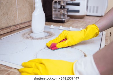 Hands wearing yellow gloves cleaning a dirty kitchen stove with a sponge, cleanliness and household chores - Powered by Shutterstock