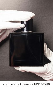 Hands In White Gloves Holding Glass Perfume Bottle Men's Cologne On A Gray Background.