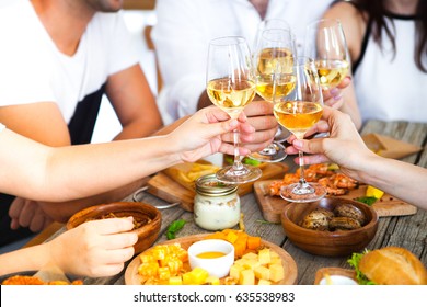 Hands With White Wine Toasting Over Served Table With Food. Friends Happiness Enjoying Dinning Eating Concept.