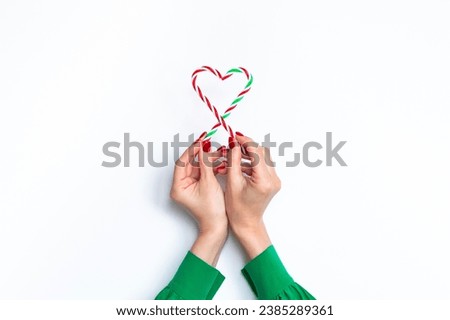 Hands of a white woman in green silk blouse holding red and green Christmas candy canes over white background