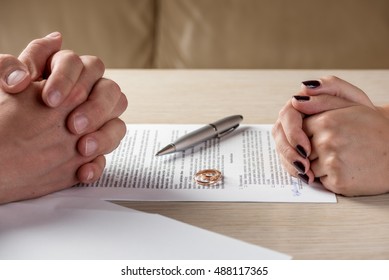 Hands of wife and husband signing divorce (dissolution, canceling marriage, legal separation) documents, filing divorce papers or premarital agreement prepared by lawyer. Wedding ring in the center

