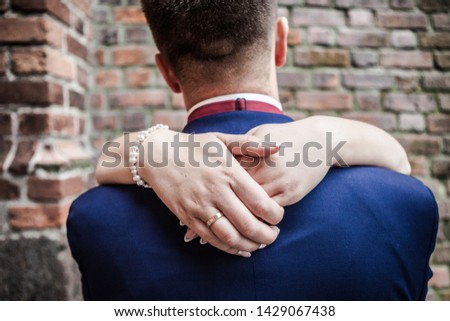 Hands of a woman around man's neck, bridal pair kissing
