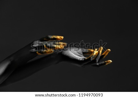 Hands of woman with black and golden paint on her skin against dark background