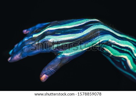 Hands of woman with blue and green paint on her skin against dark background
