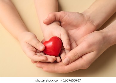 Hands Of Woman And Child With Red Heart On Color Background. Cardiology Concept