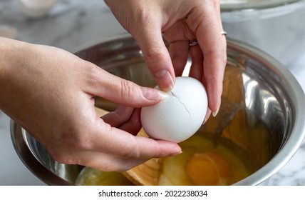 Hands Of A Woman Cracking An Egg Over A Round Metal Mixing Bowl