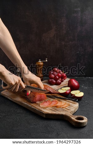 Hands of a woman cut a slice of air dried turkey ham on wooden cutting board