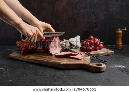Hands of a woman cut a slice of air dried pork ham on wooden cutting board