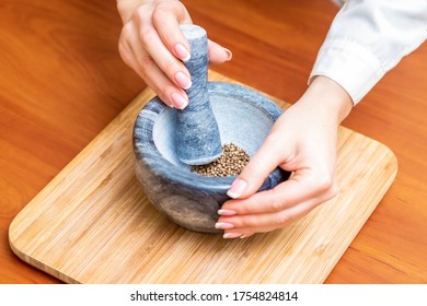 Hands of woman grinding black pepper by pestle in a gray granite mortar on the table. - Powered by Shutterstock