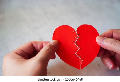 Hands Of Woman Hold And Heal Broken Heart Made From Red Paper By Stapler ,on White Concrete Background, Represent  Love , Care , Healing Heart And Recover From Pain Of Heartbreak Between Couple