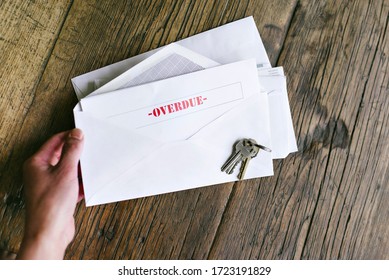Hands of a woman hold an letter with that reads Overdue in an envelope - Keys - Table - Late Payment - Shutterstock ID 1723191829