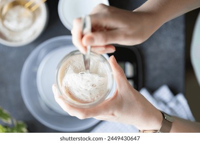 Hands of woman holding glass jar with sourdough starter. Breadmaking at home, baking artisan bread, feeding and maintaining sourdough starter. Scales, water and flour on kitchen counter, top view - Powered by Shutterstock