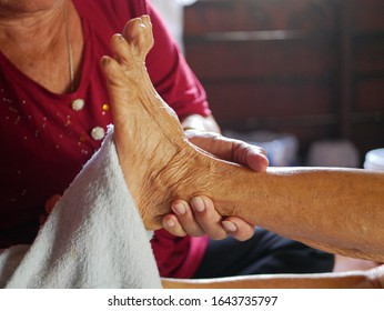 Hands of a woman holding an older person's feet, while gently wiping / cleaning it with a wet washcloth - giving an elderly a bed bath at home