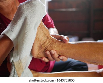 Hands of a woman holding an older person's feet, while gently wiping / cleaning it with a wet washcloth - giving an elderly a bed bath at home