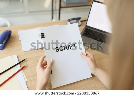 Hands of woman holding script papers for filming TV show. Female actress examines own role sitting at wooden table near laptop in office