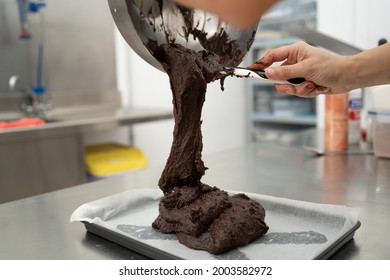 Hands of a woman in a kitchen pouring chocolate from a bowl onto a pan to bake a brownie. Concept of cooking, pastry.