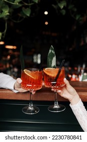 hands of woman and man are clinking, cheers with glasses of Spritz cocktail. Couple celebrating wedding, anniversary with Aperol spritz cocktails, with orange and greens Refreshing alcoholic drink. - Shutterstock ID 2230780841