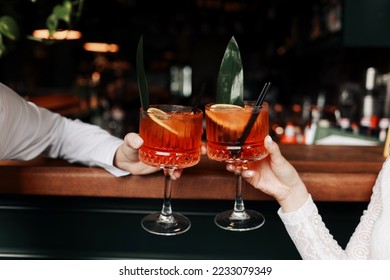 hands of woman and man are clinking, cheers with glasses of Spritz cocktail. Couple celebrating wedding, anniversary with Aperol spritz cocktails, with orange and greens Refreshing alcoholic drink. - Powered by Shutterstock