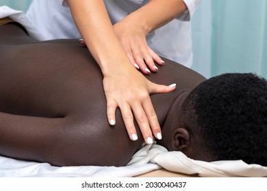 Hands Of Woman Masseuse Doing Massage Of Shoulder Area To Black Man 