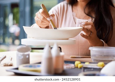 Hands, woman and painting ceramics for creativity, art workshop or class with hobby, paintbrush and material. Handmade, craft and pottery lesson with watercolor for clay bowl, design and recreation - Powered by Shutterstock