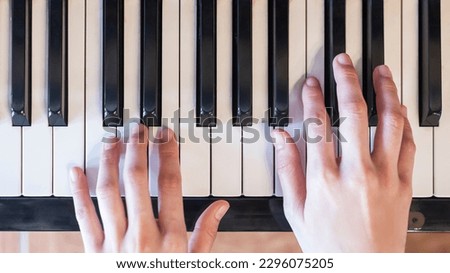 Hands of woman playing grand piano in musical school.Two hand with different level and keyboard.Blur background.Female pianist hands on grand piano keyboard.Playing music or song at home.Top view.