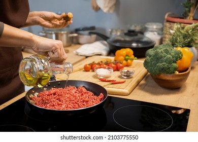 Hands Of Woman Pouring Olive Oil Into Frying Pan With Raw Minced Meat While Cooking Traditional Italian Pasta At Home