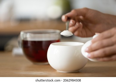 Hands Of Woman Preparing Sweet Tea, Holding Spoon, Pouring Sugar Powder Into Glass Mug Of Hot Drink, Adding Sweetener Or Fructose To Beverage. Daily Drink, Unhealthy Food Concept. Closeup.