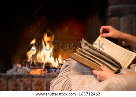 hands of woman reading book at fireplace