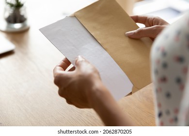Hands of woman receiving letter, invitation, notification, postcard, taking out document for reading, opening envelope with blank folded paper at work desk. Mail concept. Close up, cropped shot