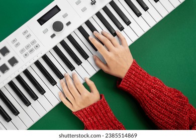 Manos de una mujer con un suéter rojo tocando el piano en un fondo verde, tumbada plana.
