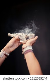 The hands of a woman shaman holding sage smudge during burning cleansing ritual. 