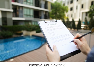 Hands of woman sign contract on background of new apartments. concept of an agreement between people, business trip. Front used with Open Font License