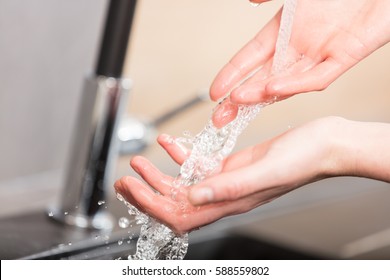 hands of a woman with some water flowing through her fingers refreshing and washing while she's in her kitchen