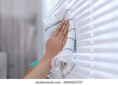 Hands of the woman uses fabric and water spray to clean the window blind - Powered by Shutterstock