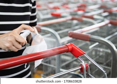 Hands of woman using spraying alcohol antiseptic,disinfecting spray,cleaning on shopping cart,trolley handle,protection during Coronavirus pandemic,Covid-19,wipe clean the surfaces with disinfectant