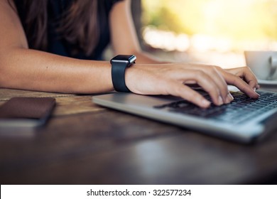 Hands Of Woman Wearing Smartwatch On The Keyboard Of Her Laptop Computer. Female Working On Laptop In A Cafe.