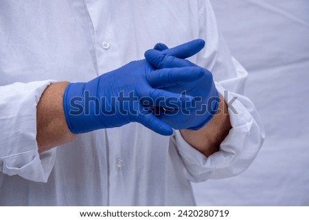 Hands of a woman in a white coat and blue latex gloves. The concept of security. Worker in blue gloves.