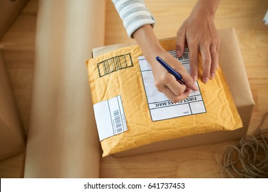 Hands of woman writing address on first class mail package - Shutterstock ID 641737453