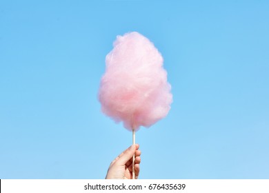 The hands of women holding pink cotton candy in the background of the blue sky