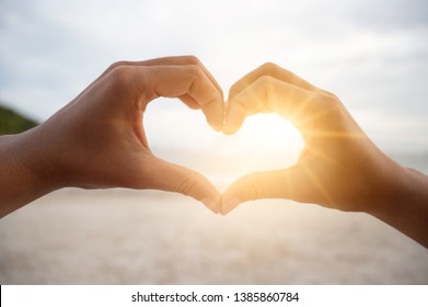 The hands of women and men are the heart shape with the sun light passing through the hands